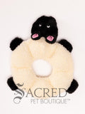 A plush dog toy resembling a sheep in neutral white and black colours, placed on a white surface, with the brand 'Sacred Pet Boutique' visible.