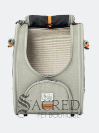 Person carrying a pet carrier with a cat inside, with a dog. surrounded by greenery, featuring the watermark 'Sacred Pet Boutique'.