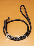 A black soft round leather dog leash with a metal clasp. Leashes are 122cm long and the leather has a diameter of 1cm. Image displayed on a golden background with 'SACRED PET BOUTIQUE' watermark.