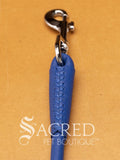 A blue soft round leather dog leash with a metal clasp. Leashes are 122cm long and the leather has a diameter of 1cm. Image displayed on a golden background with 'SACRED PET BOUTIQUE' watermark.
