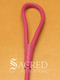 A pink soft round leather dog leash with a metal clasp. Leashes are 122cm long and the leather has a diameter of 1cm. Image displayed on a golden background with 'SACRED PET BOUTIQUE' watermark.
