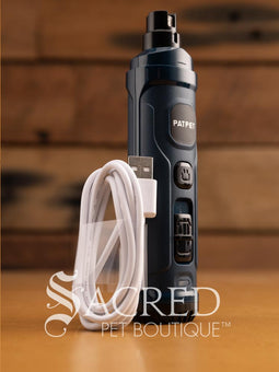 A black cordless 2-speed nail grinder for pets with a USB charging cord, placed on a wooden surface. Features Sacred Pet Boutique watermark.