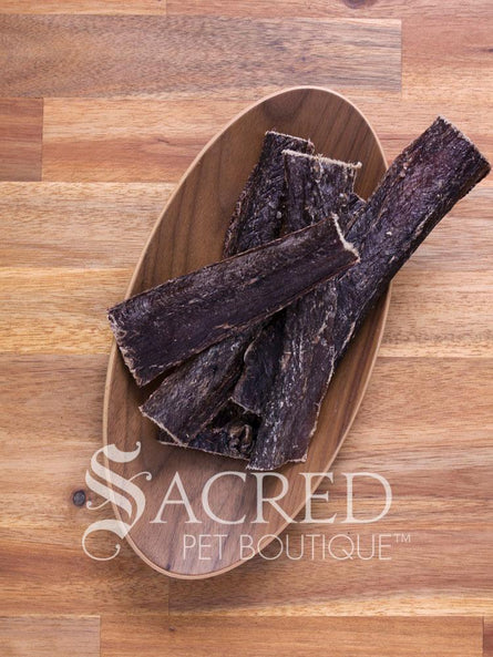 Five strips of 100% Australian beef jerky in an oval shaped bamboo dish that sits on a wooden surface. These dog treats look good enough to eat. They are waiting for a dog to come along and eat them up.