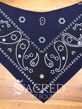 A Blue paisley dog bandana spread flat on wooden table and with a white Sacred Pet Boutique watermark