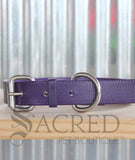 A purple biothane collar with stainless steel hardware thats buckled and lying a wooden shelf with a corrugated background. With a grey Sacred Pet Boutique watermark.