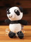 A cute crocheted panda bear stands on a wooden table with a wooden wall below. Suitable for small, toy and teacup dogs, the crochet toys squeak and will floss teeth as they play.