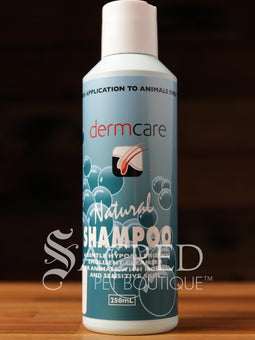 A bottle of Dermcare Natural Shampoo for animals, with a blue label and text indicating it is a hypoallergenic emollient cleanser for normal and sensitive skin. A250ml bootle on a wooden surface and features a Sacred Pet Boutique watermark.