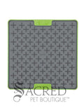 The LickiMat Tuff Buddy is an interactive slow-feeding mat designed for dogs and cats. Unlike the flexible rubber models the Tuff variation featuress a rigid, tough polypropylene backing with non-slip rubber feet. This image shows a grey cross-maze texturing paired with a durable green base. Buddy, with its cross maze design is perfect for thick, sticky treats like peanut butter, wet food or soggy biscuits. There is a white background and a grey Sacred Pet Boutique watermark. 