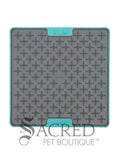 The LickiMat Tuff Buddy is an interactive slow-feeding mat designed for dogs and cats. Unlike the flexible rubber models the Tuff variation featuress a rigid, tough polypropylene backing with non-slip rubber feet. This image shows a grey cross-maze texturing paired with a durable turquoise base. Buddy, with its cross maze design is perfect for thick, sticky treats like peanut butter, wet food or soggy biscuits. There is a white background and a grey Sacred Pet Boutique watermark. 