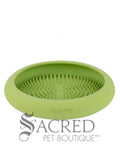 A green circular bowl shaped enrichment feeder that features small, raised rubber bristles that are designed to hold soft food or treats. It has a circular, curved design with a wide smooth outer rim which slopes inwards towards the textured centre. The name Lickimat is embossed on the front edge of the inner rim and a grey Sacred Pet Boutique watermark is at the bottom of the image. 
