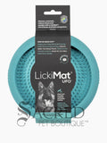 A blue circular silicone dog enrichment toy which is covered in small raised rubber bumps on the interior which is to hold soft treats. It is in its black cardboard packaging with the brand name Lickimat UFO alongside a picture of a german shepherd. This product has suction cups on the other side which can be used to stick to the floor or wall and is perfect for using to distract a dog whilst grooming them. At the bottom of the image is a grey Sacred Pet Boutique watermark. 