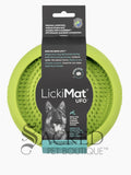 A green circular silicone dog enrichment toy which is covered in small raised rubber bumps on the interior which is to hold soft treats. It is in its black cardboard packaging with the brand name Lickimat UFO alongside a picture of a german shepherd. This product has suction cups on the other side which can be used to stick to the floor or wall and is perfect for using to distract a dog whilst grooming them. At the bottom of the image is a grey Sacred Pet Boutique watermark. 