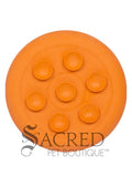 The underside of an orange circular silicone enrichment feeder displaying seven suction cups designed to stick securely to smooth horizontal or vertical surfaces like tiles, glass or refrigerators. Acts as an effective distractor during baths or grooming sessions and slows down fast eaters. A grey Sacred Pet Boutique watermark is at the bottom of the image. 