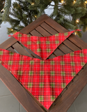 Large and small red christmas tartan dog bandanas spread flat on wooden table and with a white Sacred Pet Boutique watermark in a Christmas setting.