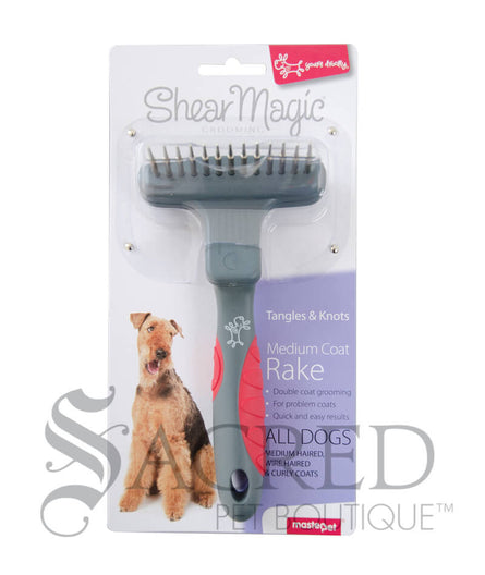 From Yours Droolly, the Shear Magic medium Coat Rake is in it's packaging showing an Airedale Terrier. The rake has a single row of spinning teeth and a red and grey handle. A Sacred Pet Boutique watermark in grey print.